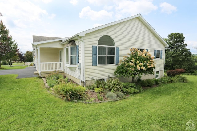 view of side of home featuring aphalt driveway, a lawn, and a porch