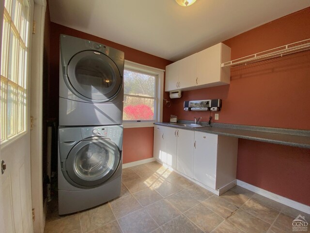 clothes washing area featuring cabinets, sink, and stacked washing maching and dryer