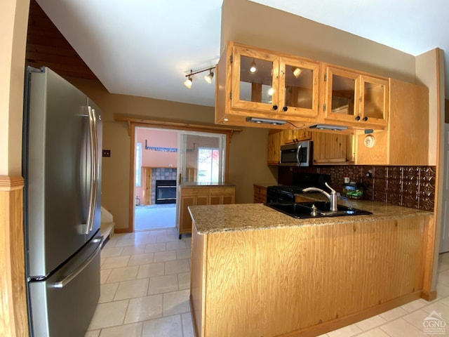 kitchen with kitchen peninsula, backsplash, stainless steel appliances, sink, and a tile fireplace