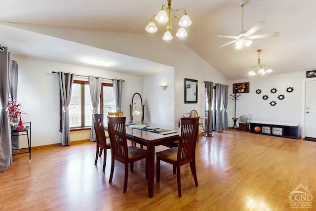 dining space with ceiling fan with notable chandelier, light wood-type flooring, baseboards, and vaulted ceiling