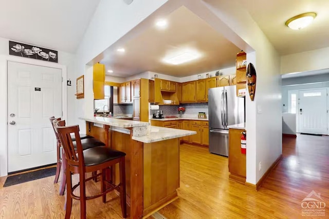 kitchen featuring backsplash, brown cabinets, a peninsula, freestanding refrigerator, and light wood-style floors