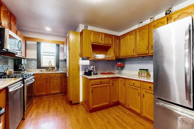 kitchen with light wood finished floors, appliances with stainless steel finishes, light countertops, and a sink