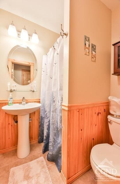 bathroom with tile patterned flooring, toilet, and wooden walls