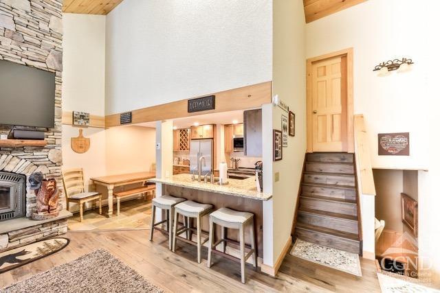 kitchen with high vaulted ceiling, white refrigerator with ice dispenser, kitchen peninsula, a breakfast bar area, and light wood-type flooring