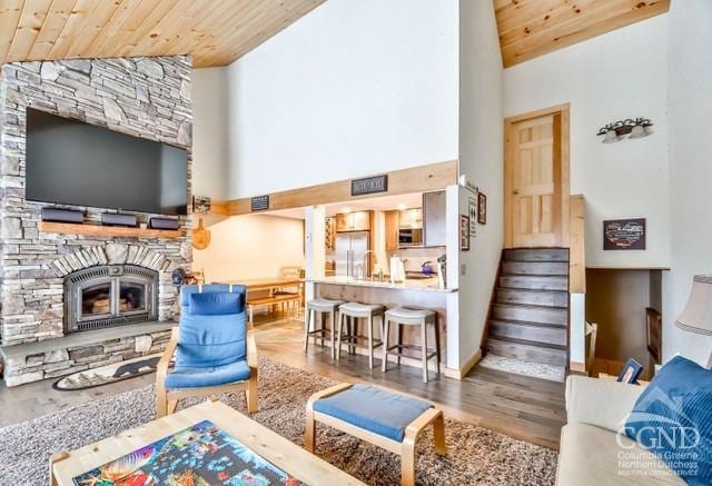 living room featuring hardwood / wood-style flooring, a stone fireplace, wooden ceiling, and high vaulted ceiling