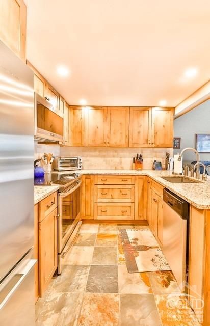 kitchen with light stone countertops, light brown cabinets, stainless steel appliances, and sink