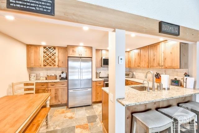 kitchen featuring sink, appliances with stainless steel finishes, tasteful backsplash, light stone counters, and a breakfast bar area