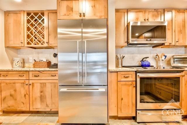 kitchen featuring light stone countertops, light brown cabinetry, appliances with stainless steel finishes, and tasteful backsplash