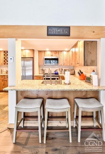 kitchen featuring kitchen peninsula, light brown cabinets, stainless steel appliances, and sink