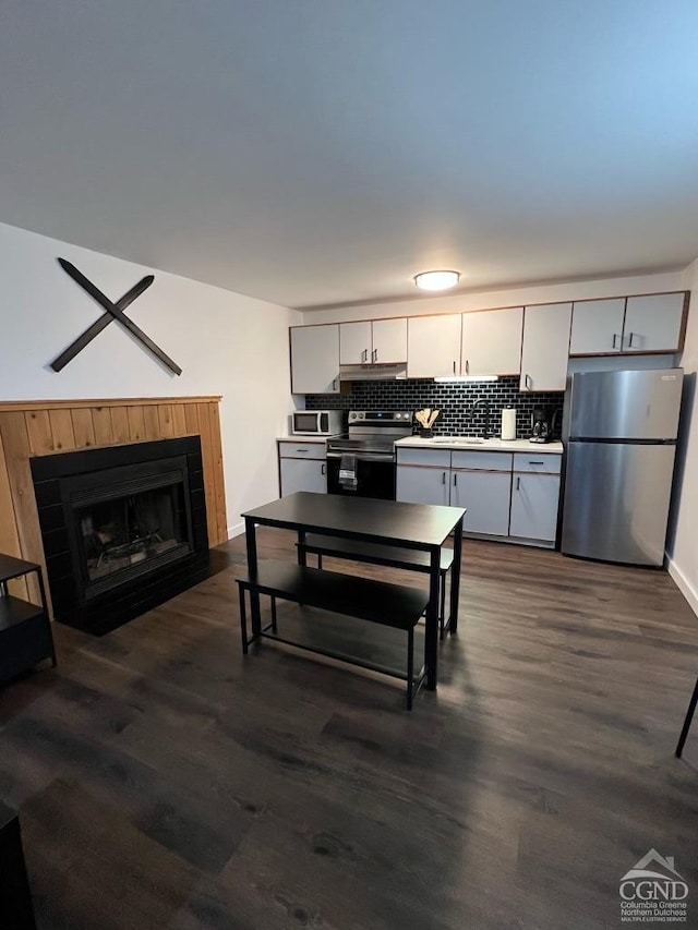 kitchen with tasteful backsplash, gray cabinetry, dark wood-type flooring, and appliances with stainless steel finishes