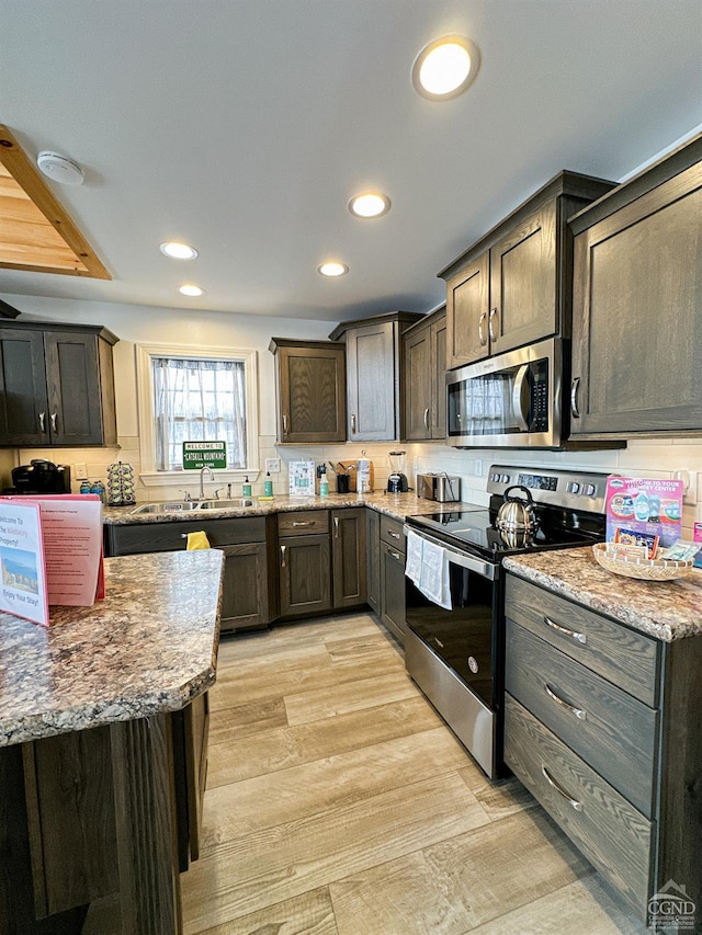 kitchen with light stone countertops, dark brown cabinets, light wood-type flooring, and stainless steel appliances