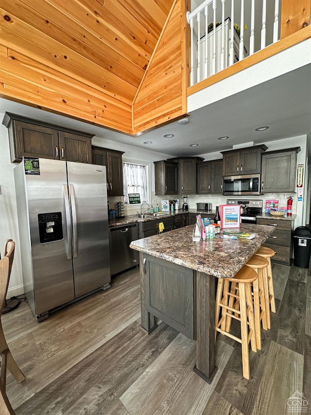 kitchen featuring a center island, high vaulted ceiling, appliances with stainless steel finishes, a kitchen bar, and dark brown cabinetry