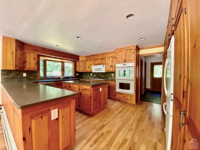 kitchen featuring tasteful backsplash, light hardwood / wood-style flooring, a center island, and white appliances