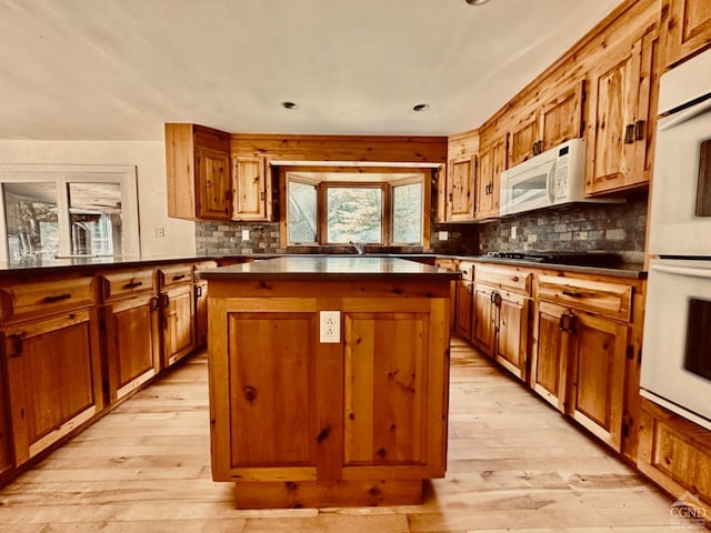 kitchen with decorative backsplash, a kitchen island, white appliances, and light wood-type flooring