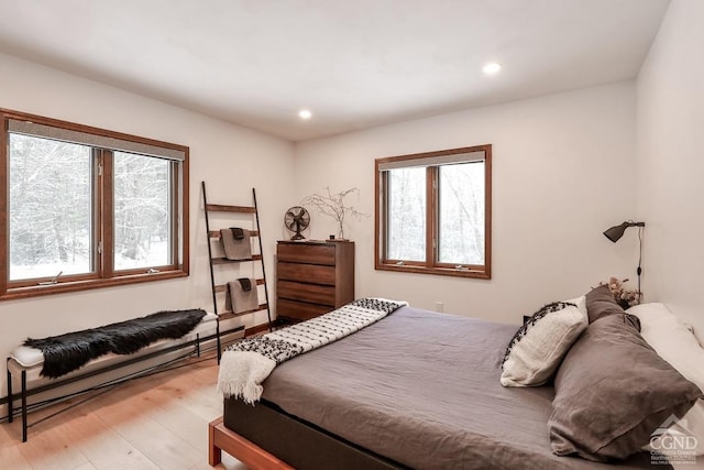 bedroom with light hardwood / wood-style floors, multiple windows, and a baseboard heating unit