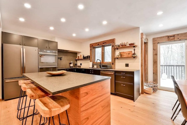 kitchen with a wealth of natural light, a center island, stainless steel appliances, a kitchen breakfast bar, and light hardwood / wood-style floors