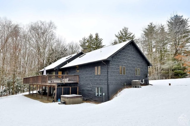 snow covered property featuring central air condition unit, a wooden deck, and a hot tub