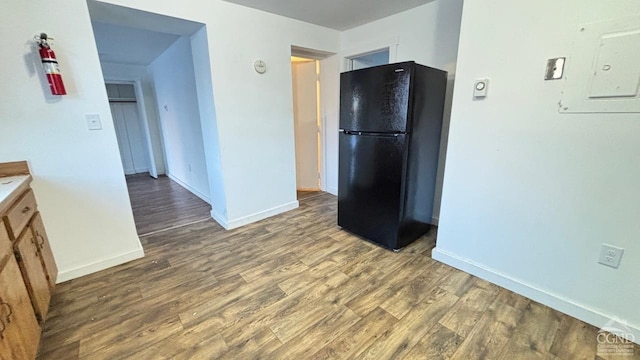 kitchen featuring baseboards, brown cabinetry, wood finished floors, freestanding refrigerator, and light countertops