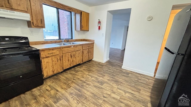 kitchen with light countertops, black range with electric stovetop, freestanding refrigerator, a sink, and under cabinet range hood