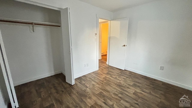 unfurnished bedroom featuring dark wood-style floors, baseboards, and a closet