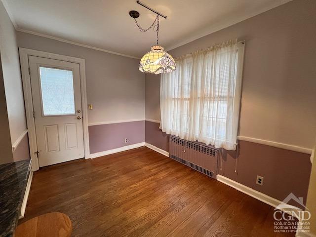 unfurnished dining area with dark wood-type flooring, ornamental molding, radiator, and baseboards