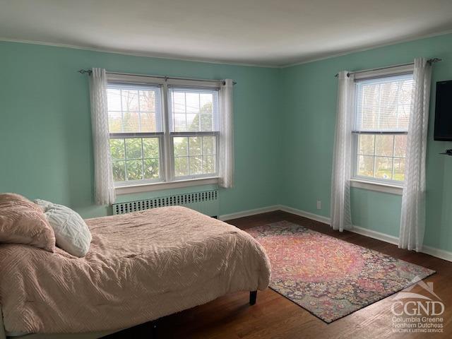 bedroom featuring radiator heating unit, baseboards, and wood finished floors