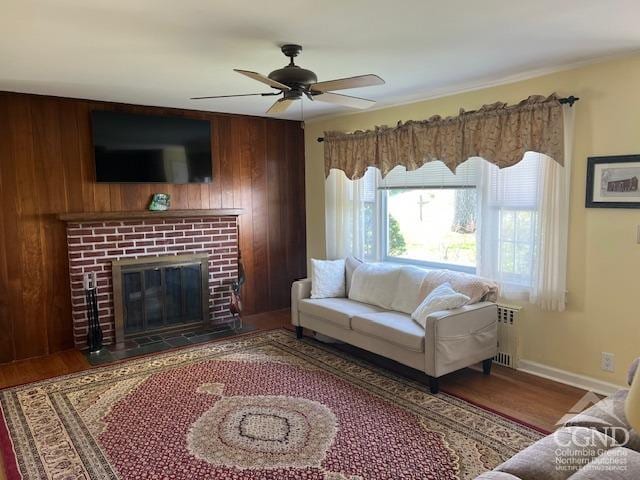 living area with a brick fireplace, wood finished floors, baseboards, ceiling fan, and wooden walls