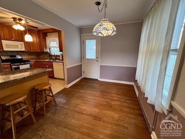 kitchen with dark countertops, a sink, white appliances, decorative light fixtures, and wood finished floors