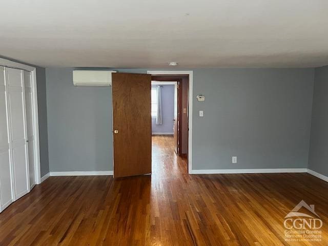 empty room featuring baseboards, a wall mounted AC, and wood finished floors