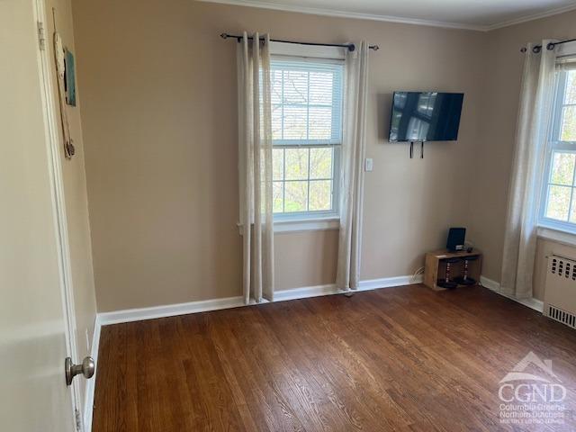 interior space with baseboards, radiator, crown molding, and wood finished floors