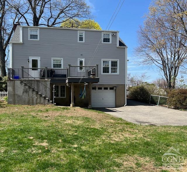 rear view of house featuring a garage, driveway, a deck, a yard, and stairway