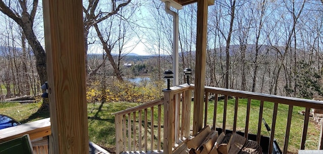 wooden deck featuring a water and mountain view, a forest view, and a yard