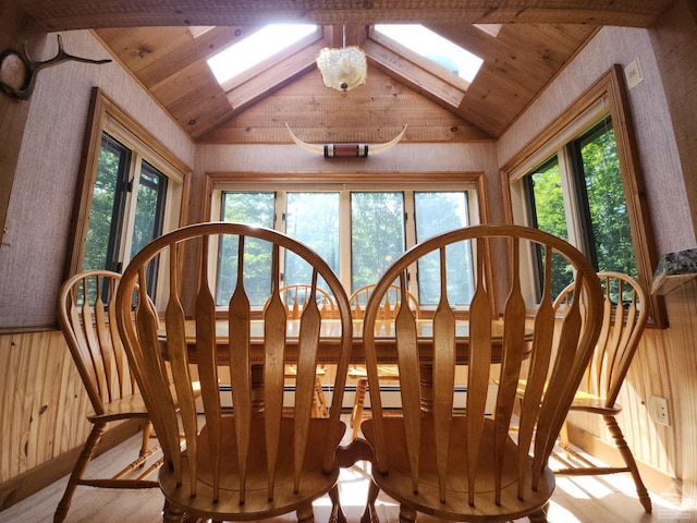 dining space featuring light hardwood / wood-style flooring, lofted ceiling with skylight, and wood walls