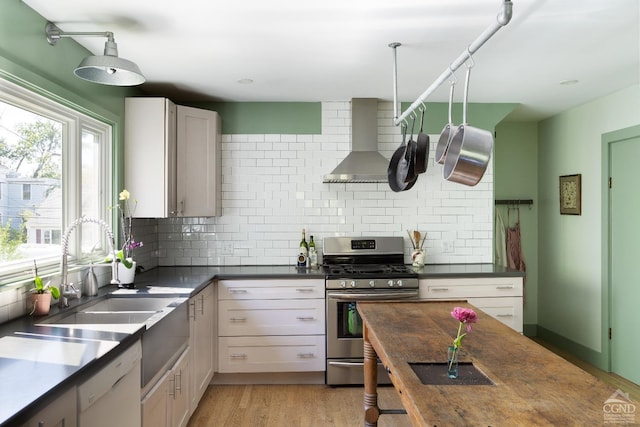 kitchen with white cabinets, wall chimney range hood, tasteful backsplash, sink, and stainless steel gas range oven