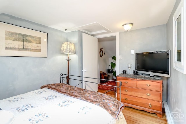 bedroom featuring attic access, light wood-style flooring, and baseboard heating
