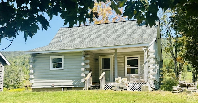 back of house featuring a lawn, a porch, log exterior, and a shingled roof