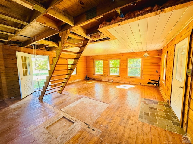 unfurnished living room featuring stairway, hardwood / wood-style flooring, and wood walls
