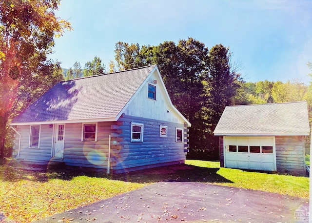 view of property exterior featuring log siding, a garage, an outdoor structure, aphalt driveway, and a yard