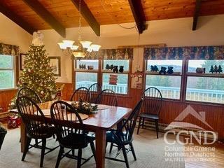 carpeted dining area with lofted ceiling with beams, wooden walls, wooden ceiling, and a notable chandelier