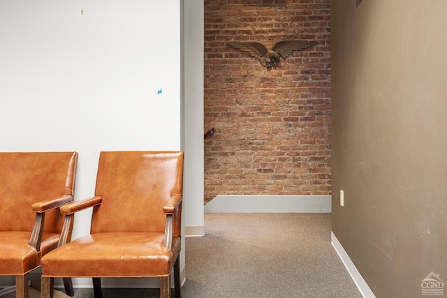 sitting room featuring carpet, baseboards, and brick wall