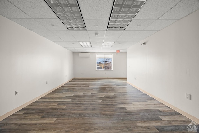 empty room with baseboards, wood finished floors, a drop ceiling, and a wall unit AC