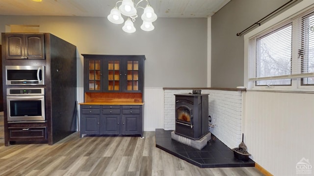 living room with an inviting chandelier, light hardwood / wood-style flooring, a wood stove, and wooden walls