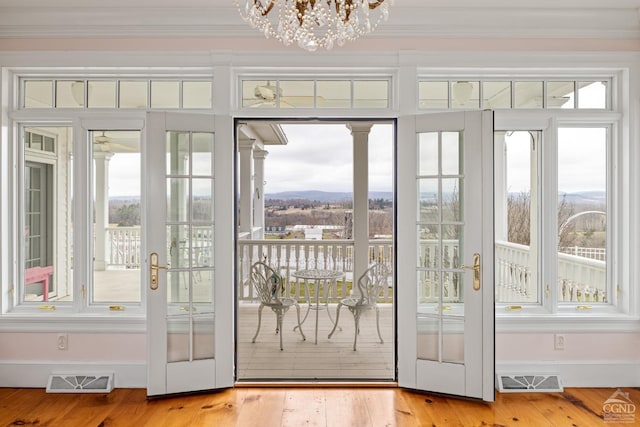 doorway with a notable chandelier, light wood-type flooring, and ornamental molding