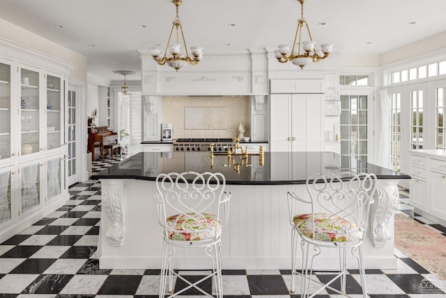 kitchen with a breakfast bar, backsplash, a spacious island, decorative light fixtures, and white cabinetry