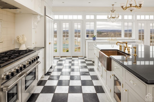 kitchen with pendant lighting, double oven range, decorative backsplash, a notable chandelier, and white cabinetry