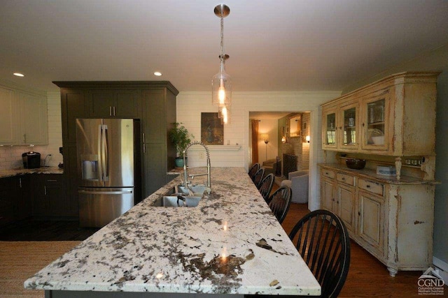 kitchen with a kitchen island with sink, sink, stainless steel fridge, and light stone counters