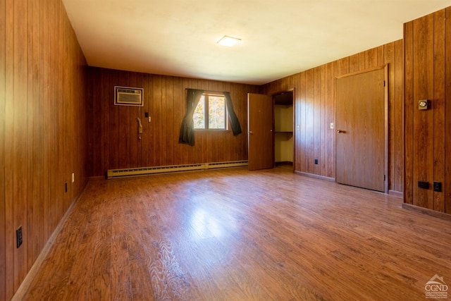 spare room with a wall mounted air conditioner, hardwood / wood-style flooring, a baseboard heating unit, and wood walls