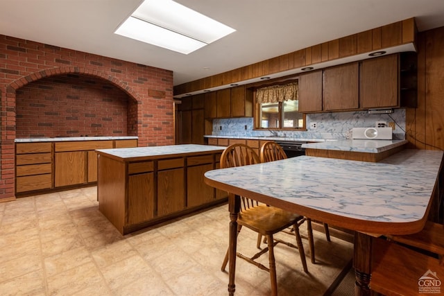 kitchen featuring decorative backsplash, dishwasher, a kitchen island, and brick wall