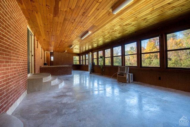 interior space featuring brick wall, wooden ceiling, wooden walls, and concrete floors