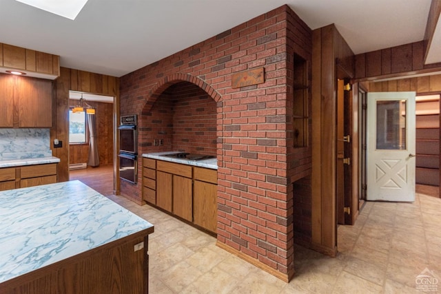 kitchen with a baseboard heating unit, wooden walls, double oven, stainless steel gas cooktop, and brick wall